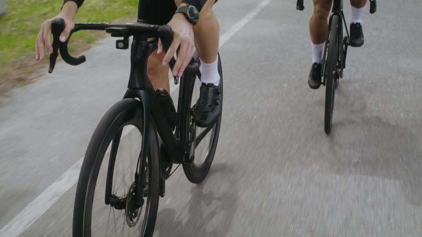 Cyclist on professional bicycle with following competitors ride along asphalt track closeup. Trained man participates in sports racing on rural road