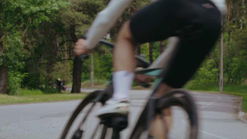Trained athletes in sportswear ride bicycles along curved road. Athletic men group on professional bikes competes on racing at green countryside slow motion