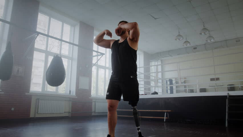 Young sportsman with prosthetic leg warms up arms before boxing training in gym. Man with disability shows determination motivation and inclusivity in sports