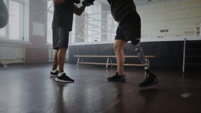 Determined sportsman with prosthetic leg after wounding attacks African American trainer in boxing gym. Athlete with disability engages in sparring fight - Powered by Shutterstock - Get 15% off with code: PIKWIZARD15