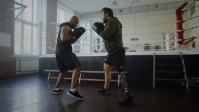 Male athlete with prosthetic leg attacks black partner during sparring in gym. Motivated man with disability fights African American trainer near boxing ring - Powered by Shutterstock - Get 15% off with code: PIKWIZARD15