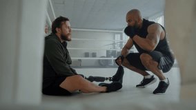 Tired boxer with prosthetic leg sits on floor as black coach motivates to fight in gym. African American friend supports frustrated man with disability in ring - Powered by Shutterstock - Get 15% off with code: PIKWIZARD15