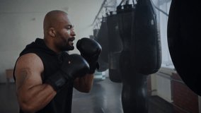 Focused African American man boxer beats heavy punching training in gym. Black bald sportsman practices strong punches with boxing equipment in fighting club - Powered by Shutterstock - Get 15% off with code: PIKWIZARD15