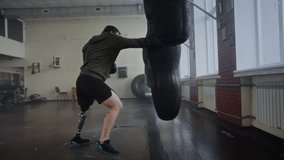 Focused athlete with prosthetic leg practices boxing punches on heavy bag in gym. Man boxer with disability demonstrates strength overcoming physical challenges - Powered by Shutterstock - Get 15% off with code: PIKWIZARD15