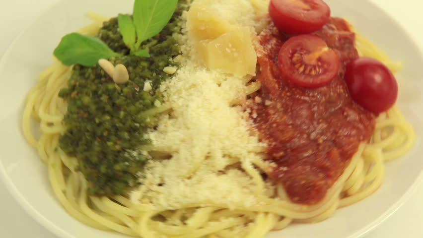 On a white plate rotates pasta. On top of pasta - Pesto, Parmesan and Tomato