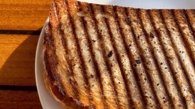 Golden grilled sandwich filled with melted cheese, tomatoes, and peppers sits warm on a white plate near at a seaside restaurant, slow motion - Powered by Shutterstock - Get 15% off with code: PIKWIZARD15