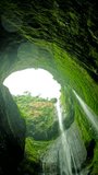View from inside a moss-covered cave looking up at waterfalls descending through a circular opening. Water cascades down rocky walls. Madakaripura Waterfall, Indonesia. - Powered by Shutterstock - Get 15% off with code: PIKWIZARD15