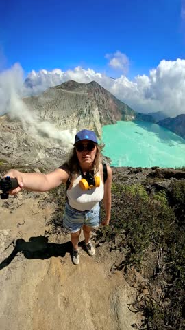 Woman taking a selfie overlooking the turquoise acidic crater lake and volcanic landscape of Ijen volcano, East Java, Indonesia.