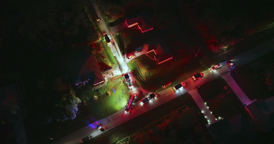 Firefighter trucks at fire alarm scene of suburban house at night. First responders with bright lights at potential fire hazard at Florida home.