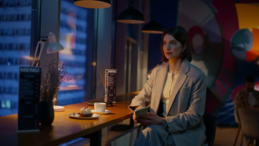 Smiling lady settling bill with smartphone in restaurant at night closeup. Confident woman enjoying dinner making cashless payment in cafe. Elegant businesswoman staring at waiter during evening meal