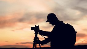 Traveler with tripod, camera takes beautiful pictures of landscape against beautiful sunny sky with clouds. Photographer with backpack uses camera with tripod against amazingly beautiful sunset - Powered by Shutterstock - Get 15% off with code: PIKWIZARD15