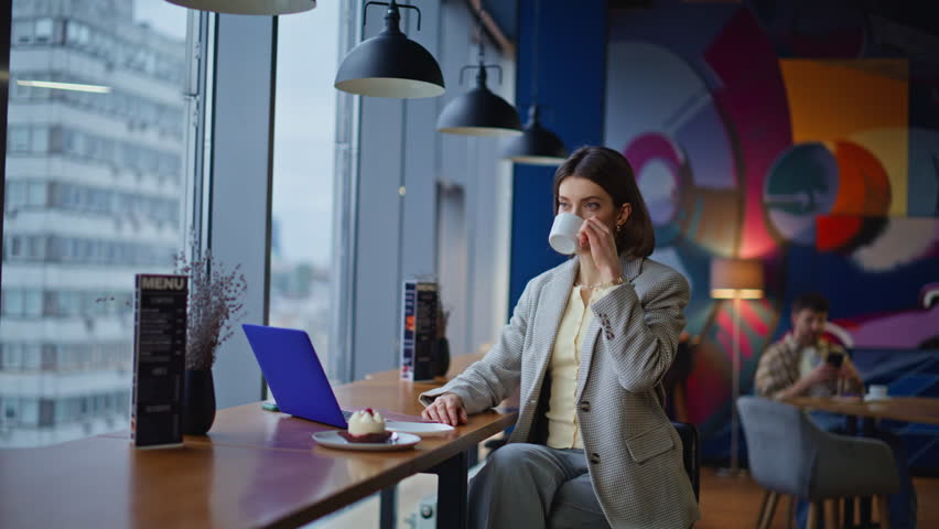 Confident businesswoman working laptop at city cafe closeup. Beautiful elegant woman drinking cappuccino sitting cafeteria table with computer. Serious manager freelancer typing email message keyboard