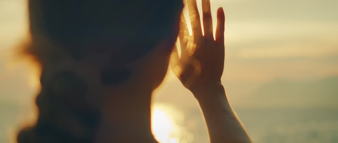 Woman raising hand to block sun while gazing at sea sunset in summer Croatia