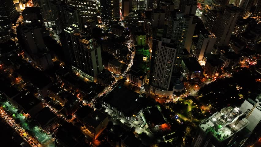 Flying over the modern buildings and colorful streets. Makati City at Night. Metro Manila. Philippines.
