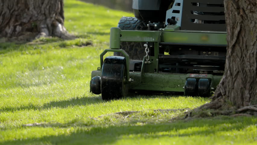 Professional cutting a grass in the park with a large lawn mower. Landscaping service scene