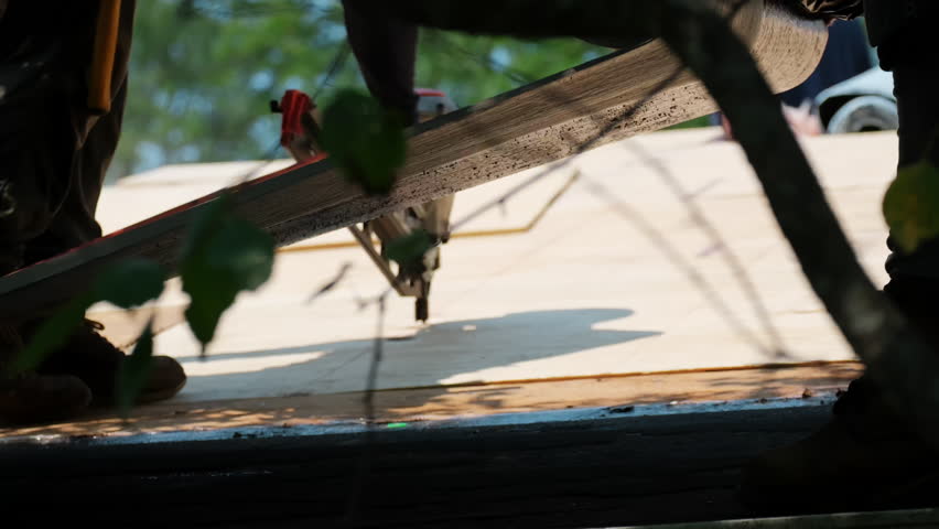 Roofers are nailing down wooden panels ant stretching the glue film on the roof of the residential house. Element of roof renovation