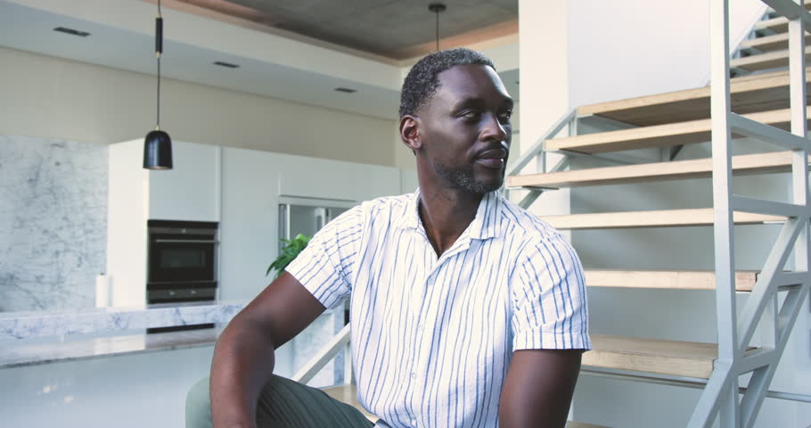 Looking left mid adult African American man gesturing to pendants, inspecting kitchen and smiling. Contemporary, lifestyle, minimalist, interior, casual, relaxed, warmth