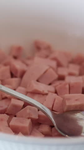 cooked sausage mortadella cubes on a white background withspoon plate