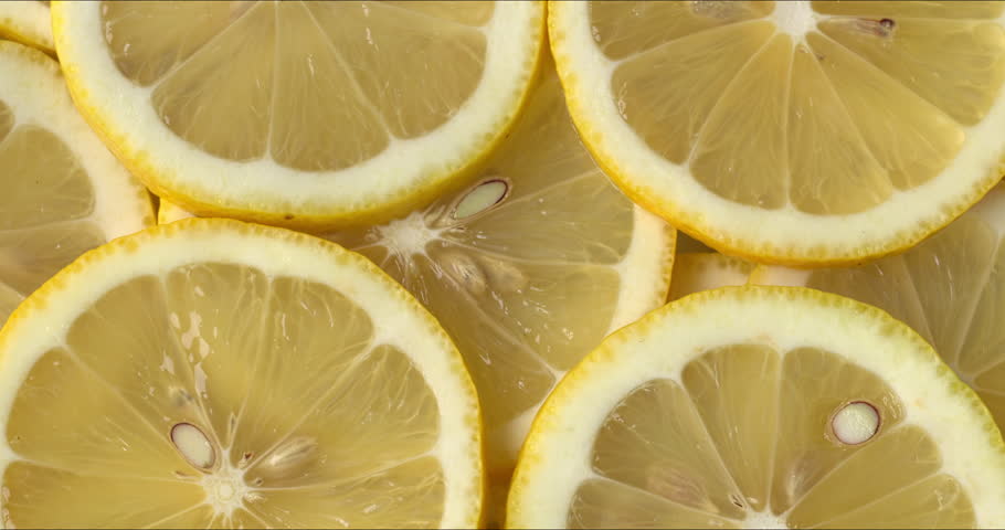 Background of sliced lemons with skin. Close-up, flat lay, zoom in while rotating.