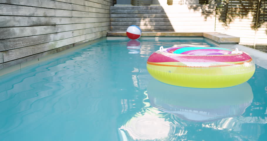 Gentle breeze is rotating ring, drifting beach ball in pool and nudging ring against fence. Playfulness, relaxation, leisure, outdoor, vibrant, summer, water