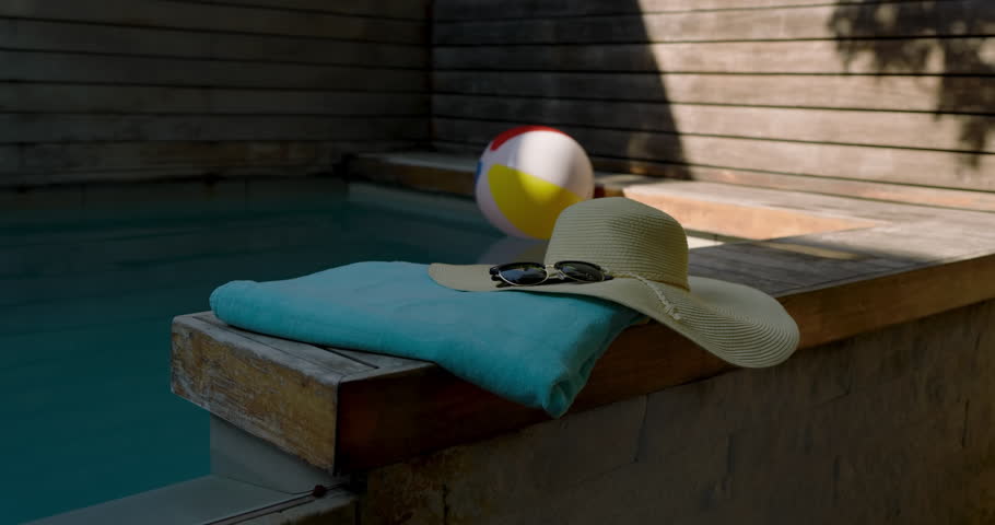 gentle breeze starting, beach ball drifting on wooden bench past towel with hat and sunglasses. Relaxation, leisure, outdoor, vacation, summer, tranquility, lifestyle