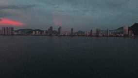 Early morning drone view from sea to coastal city. Colorful clouds at sunrise illuminate high-rise buildings forming a pattern like an equalizer along the shoreline. 4K 60FPS - Powered by Shutterstock - Get 15% off with code: PIKWIZARD15
