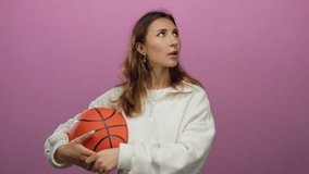 Woman holding basketball with a thoughtful expression against an isolated pink background, capturing athletic lifestyle through dynamic posing and vibrant color contrast. - Powered by Shutterstock - Get 15% off with code: PIKWIZARD15