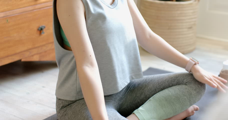 Adult Asian woman putting on white headphones and inhaling on dark yoga mat following breathwork. Meditation, mindfulness, wellness, relaxation, interior, serene, focus