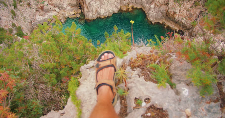 Man stands on rocky cliff edge looking down at turquoise bay in Capri summer trip