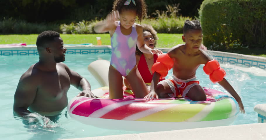 Black father with children steadying drifting swirl float while kids scrambling onto it in pool. Family fun, poolside, vibrant, recreational, leisure, joyful, summer