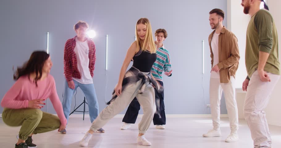 Group of energetic young adults in casual wear dancing together in bright dance studio. Happy friends enjoying choreography session while performing energetic hip hop dance. Modern dance concept.