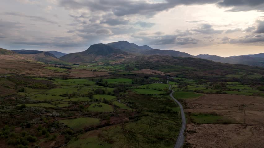 Drone video of Cadair Idris mountain in Snowdonia Wales with A470 road, valleys, grassland and ridges in the foreground during sunset.