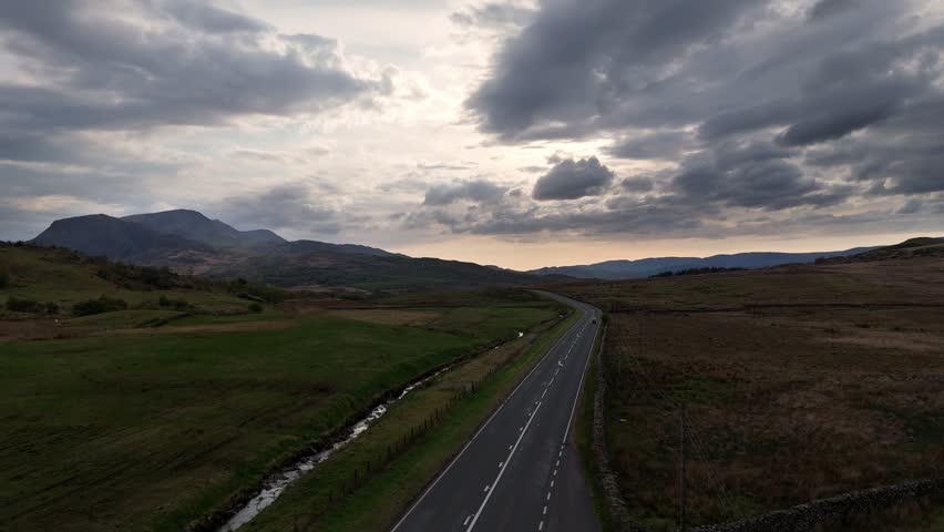 Drone video of Cadair Idris mountain in Snowdonia Wales with A470 road, valleys, grassland and ridges in the foreground during sunset.