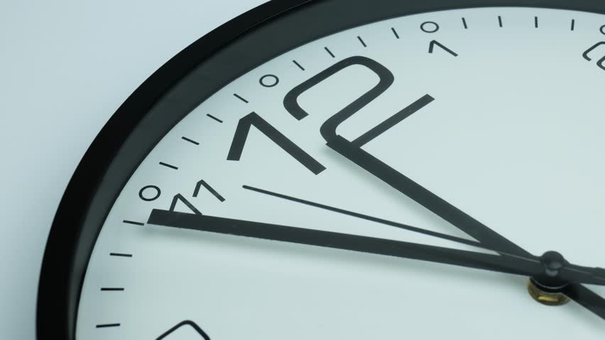 A close-up of a clock just before noon on a white background