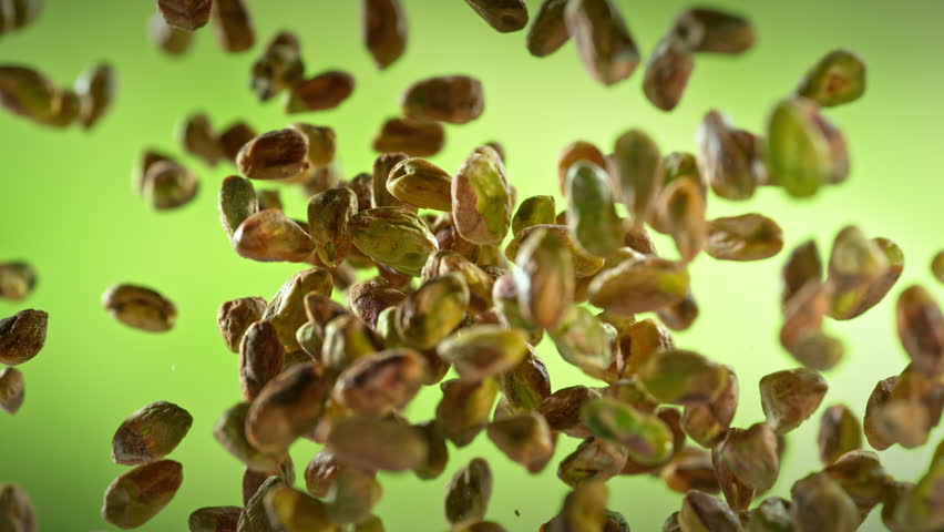 Super Slow Motion Shot of Fresh Peeled Pistachio Nuts Flying Up on Green Background at 1000fps.