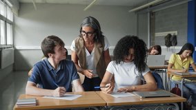 Mature female teacher helping teenager students learning writing text at College High School - Powered by Shutterstock - Get 15% off with code: PIKWIZARD15