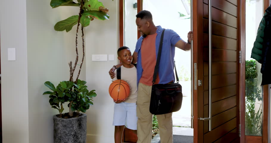 African American father and son arriving home hugging, bonding over basketball on entryway rug. Family, bonding, recreation, modern, warm, casual, interaction