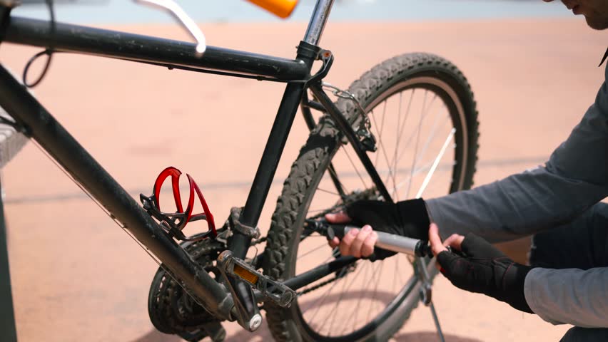 Cyclist Pumping Air Into Tire After Crash. Triathlete Fix His Bicycle After Breakdown. Cyclist Check Gears And Wheels After Cycling Race. Bicyclist Repairing Wheel. Sportsman Repair Bike Flat Tire