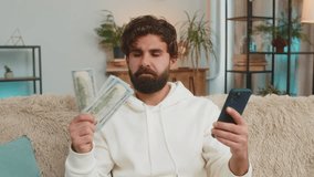 Planning budget. Rich happy Indian man using smartphone calculator app count dollar cash, calculate domestic bills at home. Guy satisfied of income earnings win saves money for planned vacation gifts. - Powered by Shutterstock - Get 15% off with code: PIKWIZARD15