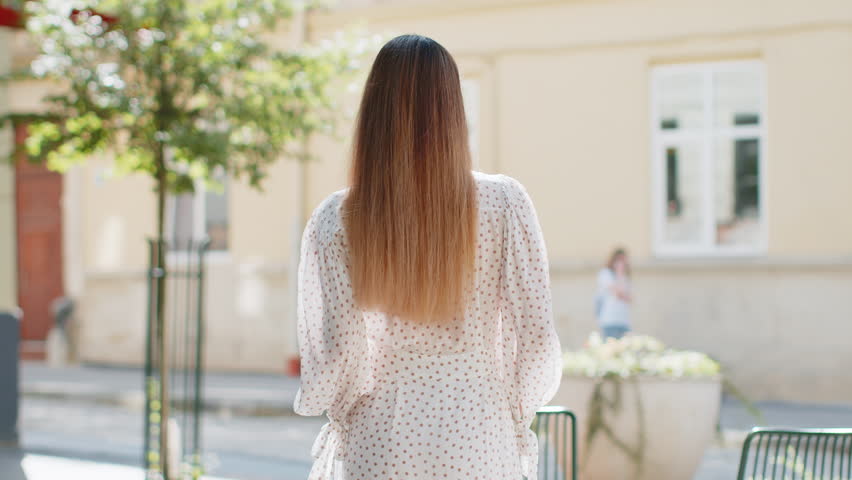 Portrait of happy woman stands with her back and turns around smiling friendly, glad expression looking at camera dreaming, resting, relaxation feel satisfied good news outdoors. Girl on city street.