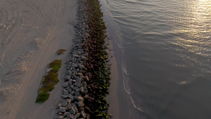 Aerial shot of rocky shoreline of Seal Beach, California at golden hour with San Gabriel River connecting with the Pacific Ocean