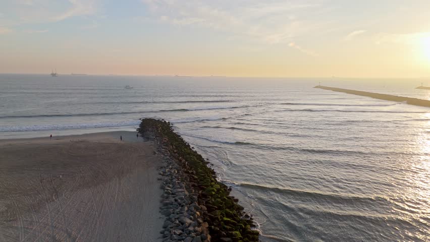 Aerial shot of rocky shoreline of Seal Beach, California at golden hour with San Gabriel River connecting with the Pacific Ocean