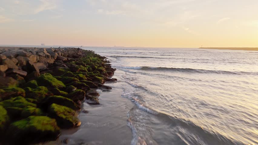 Low flyover of the San Gabriel River at golden hour with waves crashing into the rocky jetties, Seal Beach, California