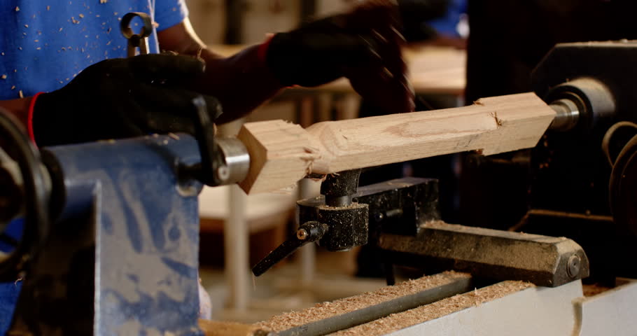 Securing wood blank on shop lathe, African American man shaping cylinder, sanding for smooth finish. Craftsmanship, woodworking, industrial, artisan, detail, workshop, precision