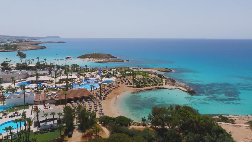 Aerial footage of Ayia Napa, Cyprus, showing turquoise waters, rocky shorelines, sparse vegetation, and winding walking paths in smooth motion.