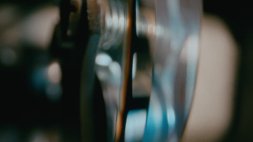 Macro close-up of a filmstrip smoothly running over a metal sprocket in a retro movie projector, showcasing vintage cinematic mechanics in action