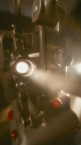 Atmospheric smoke drifts around the glowing lens of a vintage film projector, casting a dramatic light in a nostalgic cinematic setting