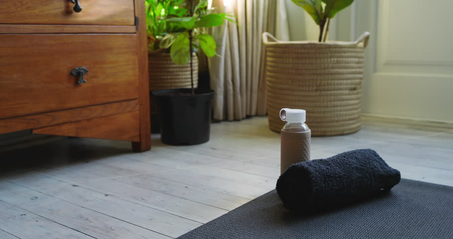 Camera shifting forward to towel and water bottle in home gym, lighting indicating exercise start. Fitness accessories, home gym, minimalist decor, wellness, motivation, natural lighting, organized