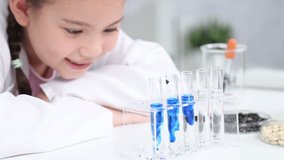 Young primary school student girl in white lab coat holding test tube with blue liquid, smiling and engaging in scientific activity, with laboratory equipment, educational science class back to school - Powered by Shutterstock - Get 15% off with code: PIKWIZARD15