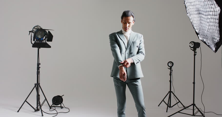 After stepping left, Asian male model walking center adjusting suit jacket in studio for modeling. Professional, fashion, minimalist, sophisticated, male, styling, portrait